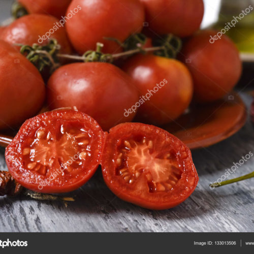 closeup of a pile of tomates de colgar, a typical spanish species of tomatoes, in an earthenware plate, on a rustic wooden table and a cruet with olive oil in the background